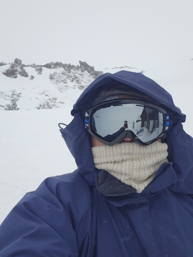 Man in waterproof jacket, scarf and goggles out in the snow.