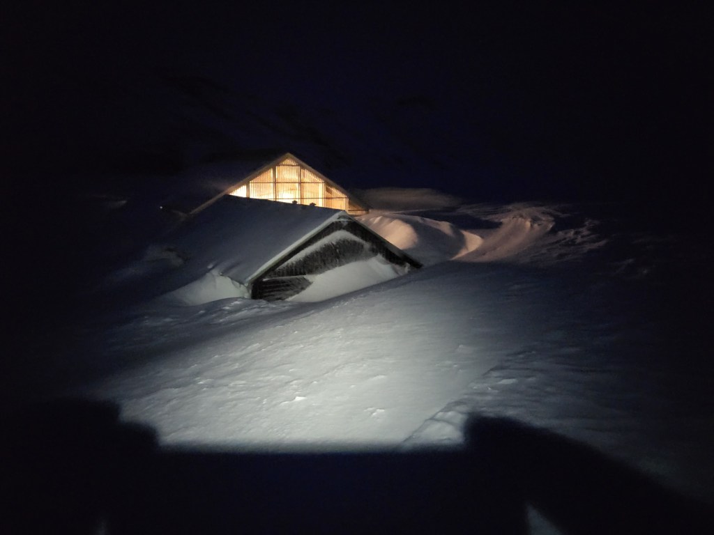 Winter hut buried in snow at night.