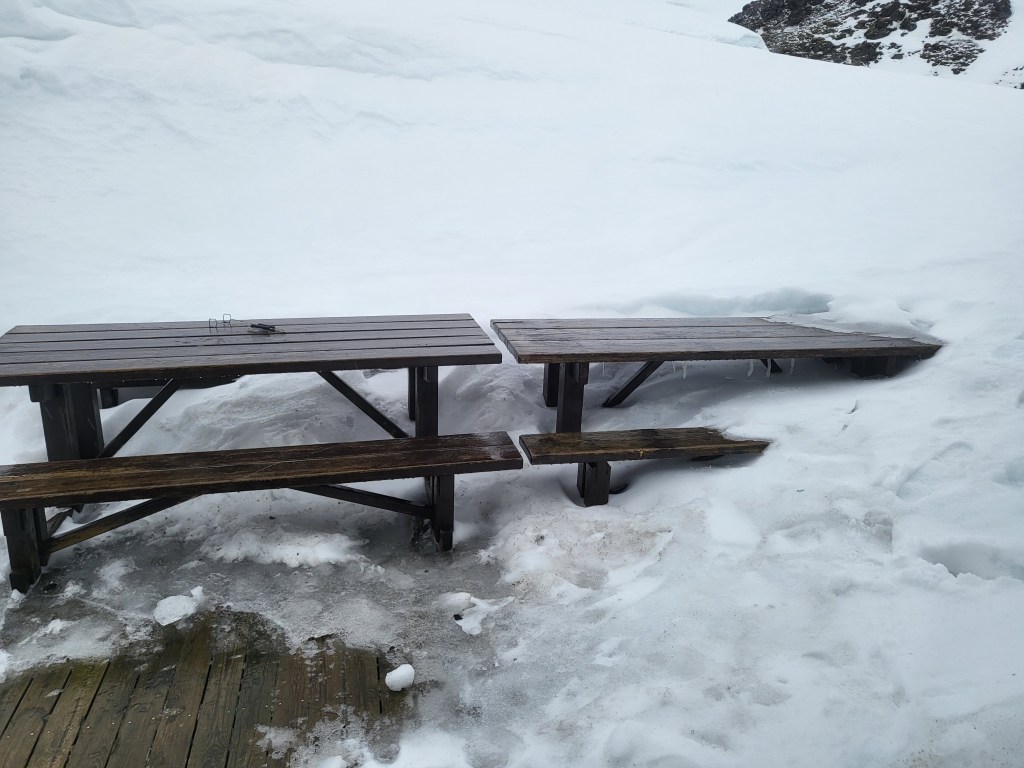 Picnic tables submerged in snow.